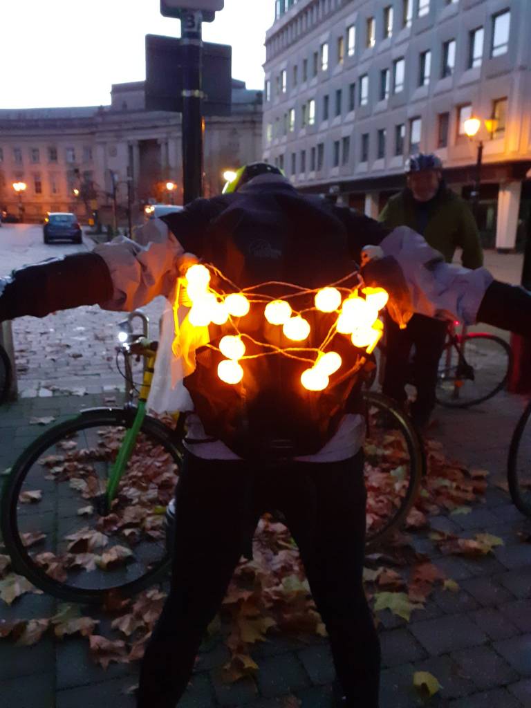 A person viewed from behind with pumpkin lights and skeletons mounted on a backpack. (Thanks to June Leece)